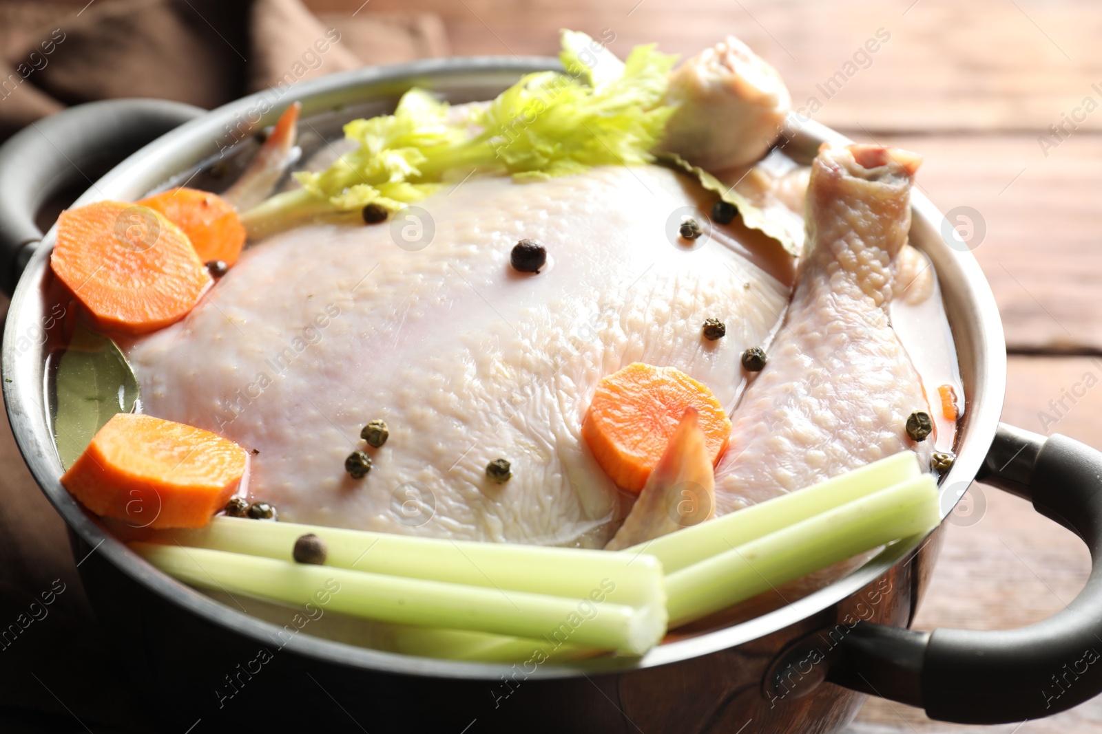 Photo of Whole raw turkey, cut carrot, celery and spices in pot on wooden table, closeup