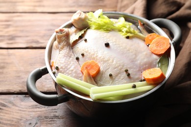 Photo of Whole raw turkey, cut carrot, celery and spices in pot on wooden table, closeup