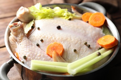 Photo of Whole raw turkey, cut carrot, celery and spices in pot on wooden table, closeup