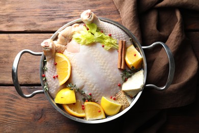 Photo of Whole raw turkey, citrus fruits and spices in pot on wooden table, top view