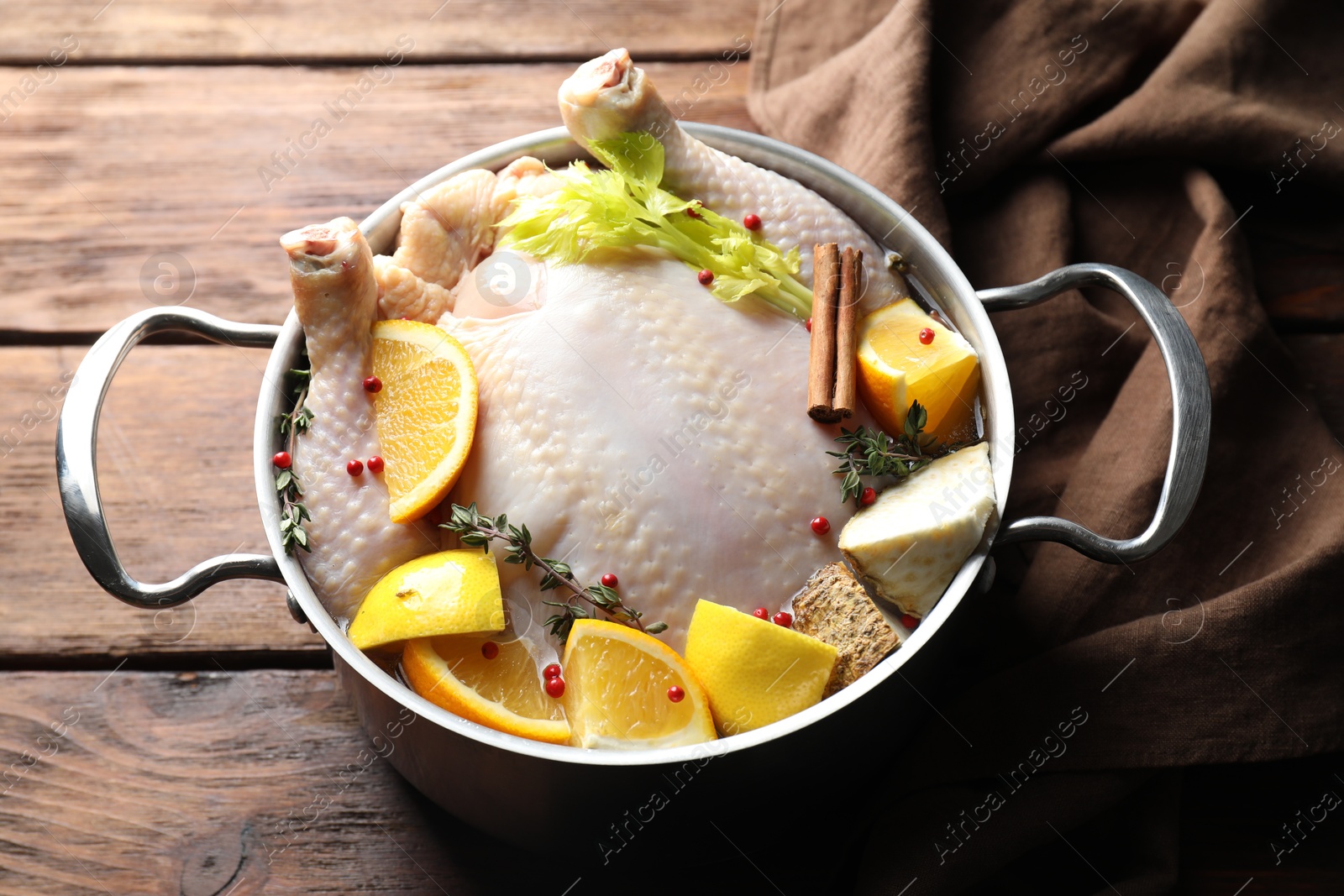 Photo of Whole raw turkey, citrus fruits and spices in pot on wooden table, closeup