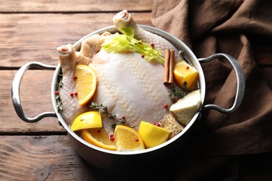 Photo of Whole raw turkey, citrus fruits and spices in pot on wooden table, closeup