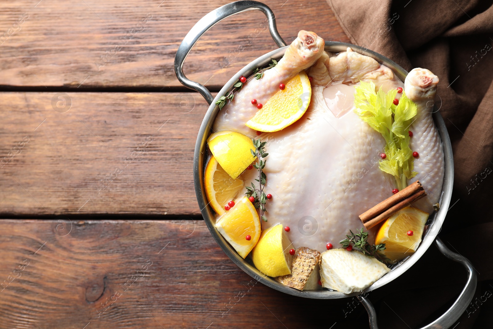 Photo of Whole raw turkey, citrus fruits and spices in pot on wooden table, top view. Space for text