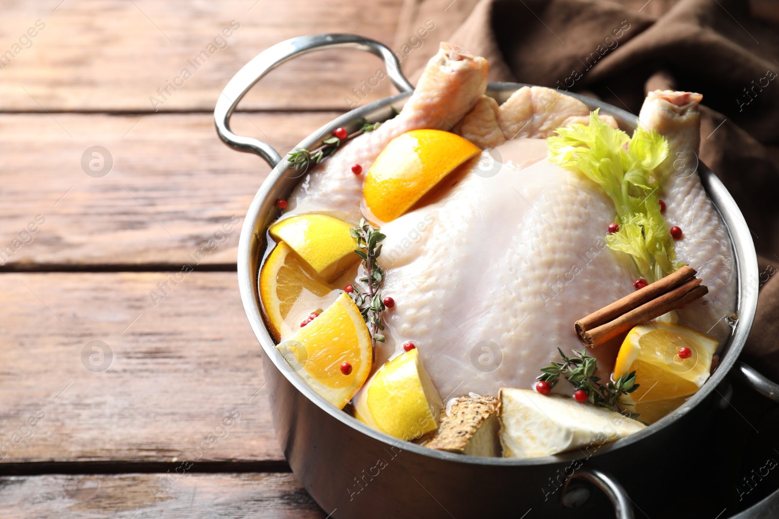 Photo of Whole raw turkey, citrus fruits and spices in pot on wooden table, closeup. Space for text