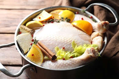 Photo of Whole raw turkey, citrus fruits and spices in pot on wooden table, closeup