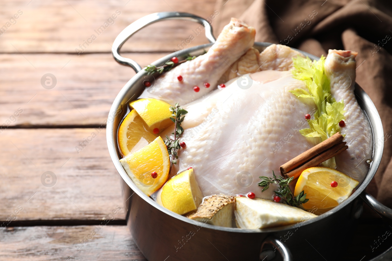 Photo of Whole raw turkey, citrus fruits and spices in pot on wooden table, closeup. Space for text