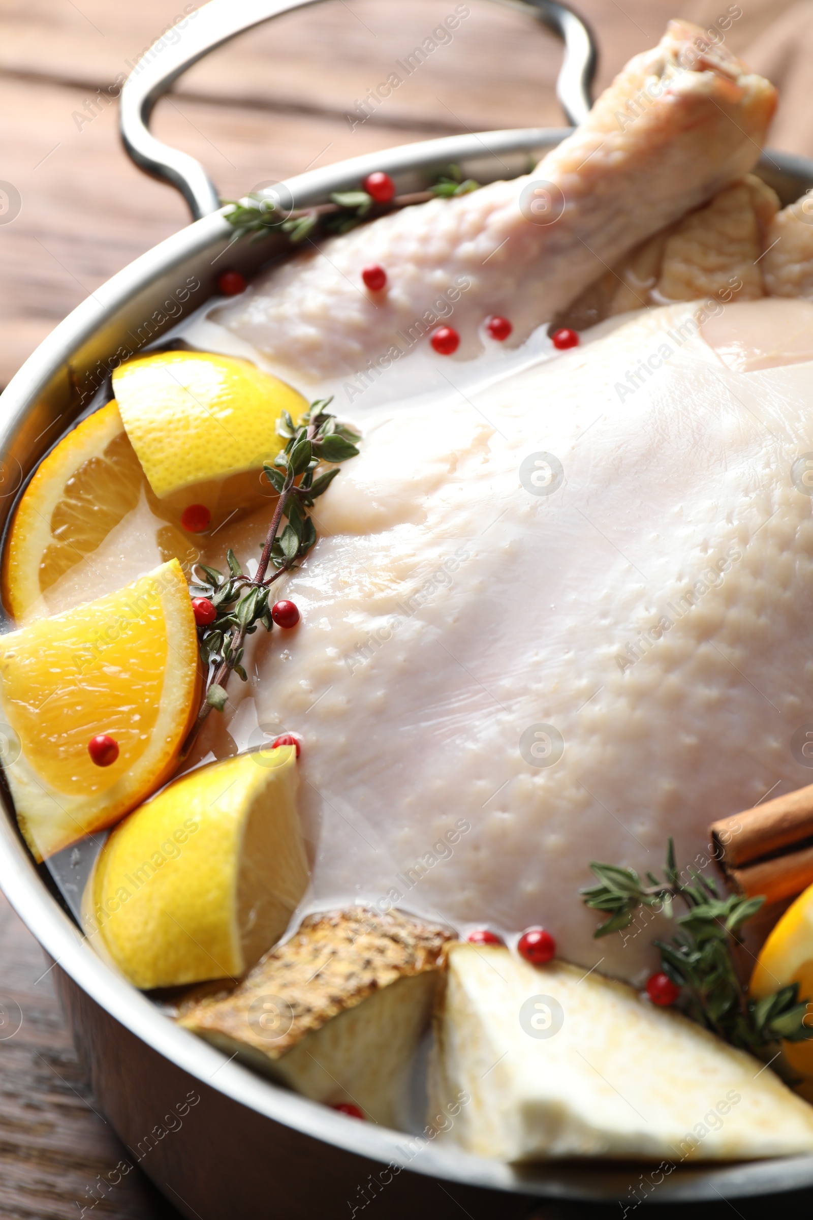 Photo of Whole raw turkey, citrus fruits and spices in pot on wooden table, closeup