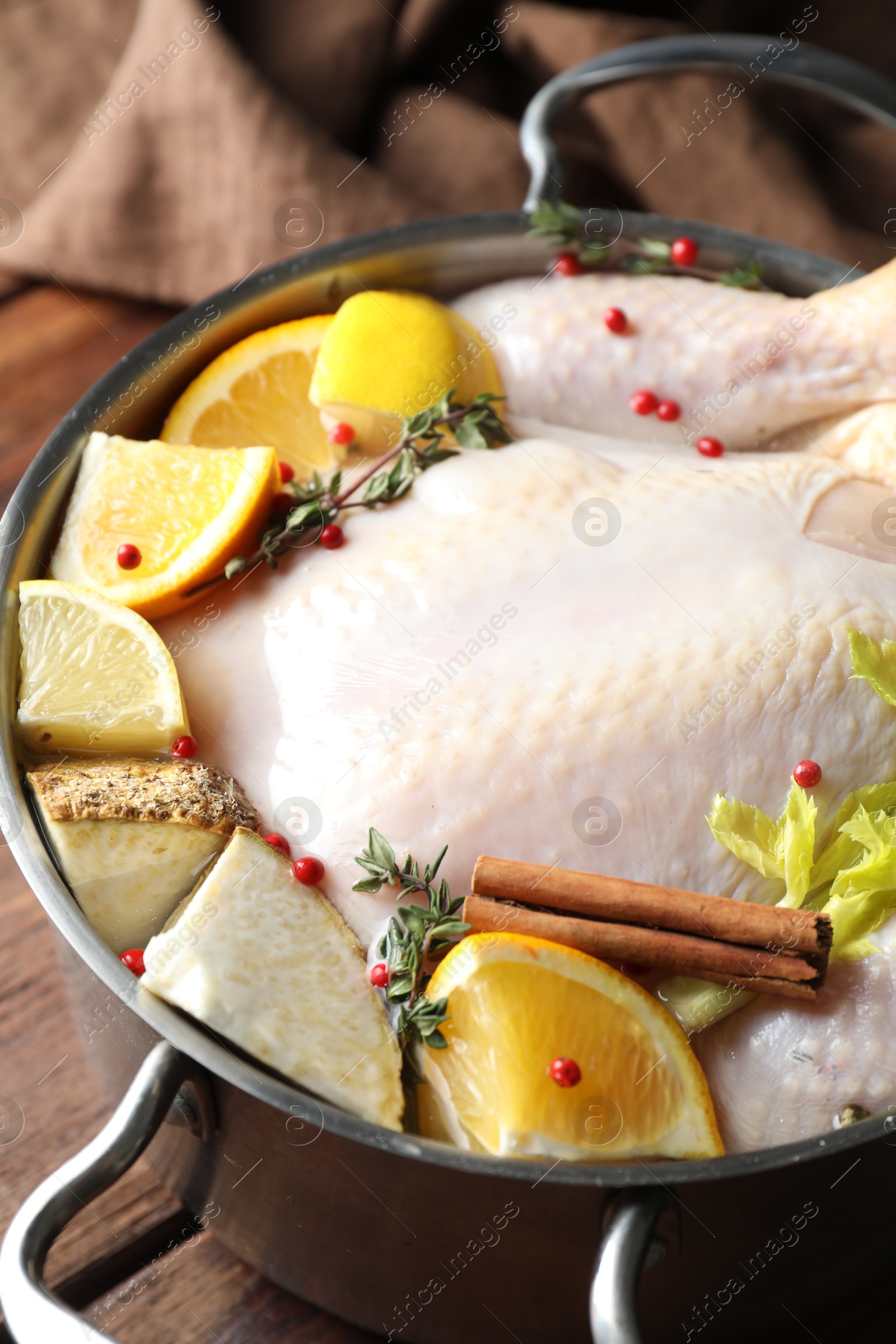 Photo of Whole raw turkey, citrus fruits and spices in pot on wooden table, closeup