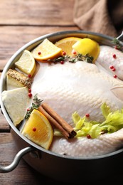 Photo of Whole raw turkey, citrus fruits and spices in pot on wooden table, closeup