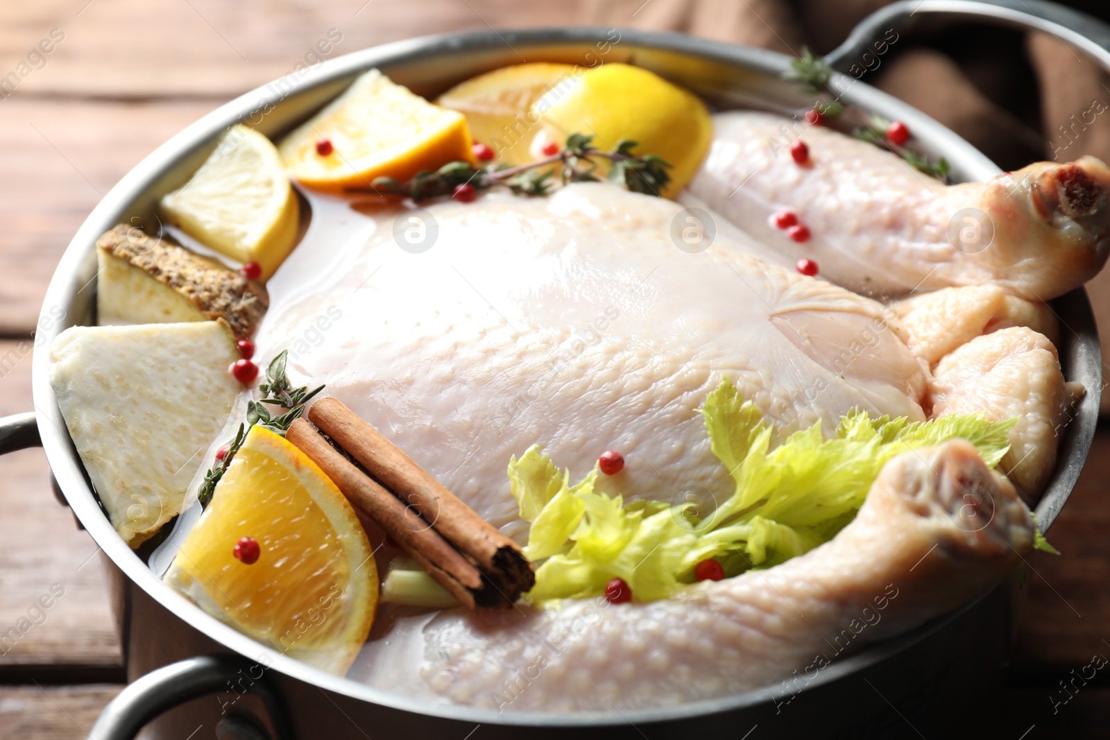 Photo of Whole raw turkey, citrus fruits and spices in pot on wooden table, closeup