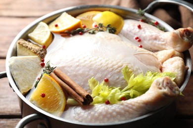 Whole raw turkey, citrus fruits and spices in pot on wooden table, closeup