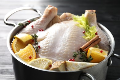 Photo of Whole raw turkey, citrus fruits and spices in pot on black table, closeup