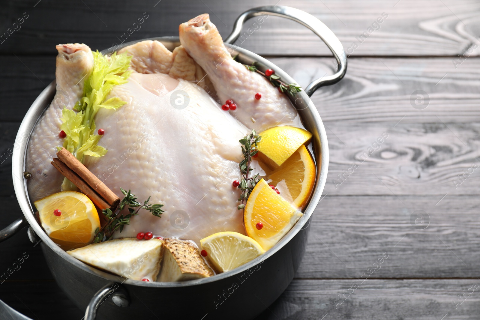 Photo of Whole raw turkey, citrus fruits and spices in pot on black wooden table, closeup. Space for text