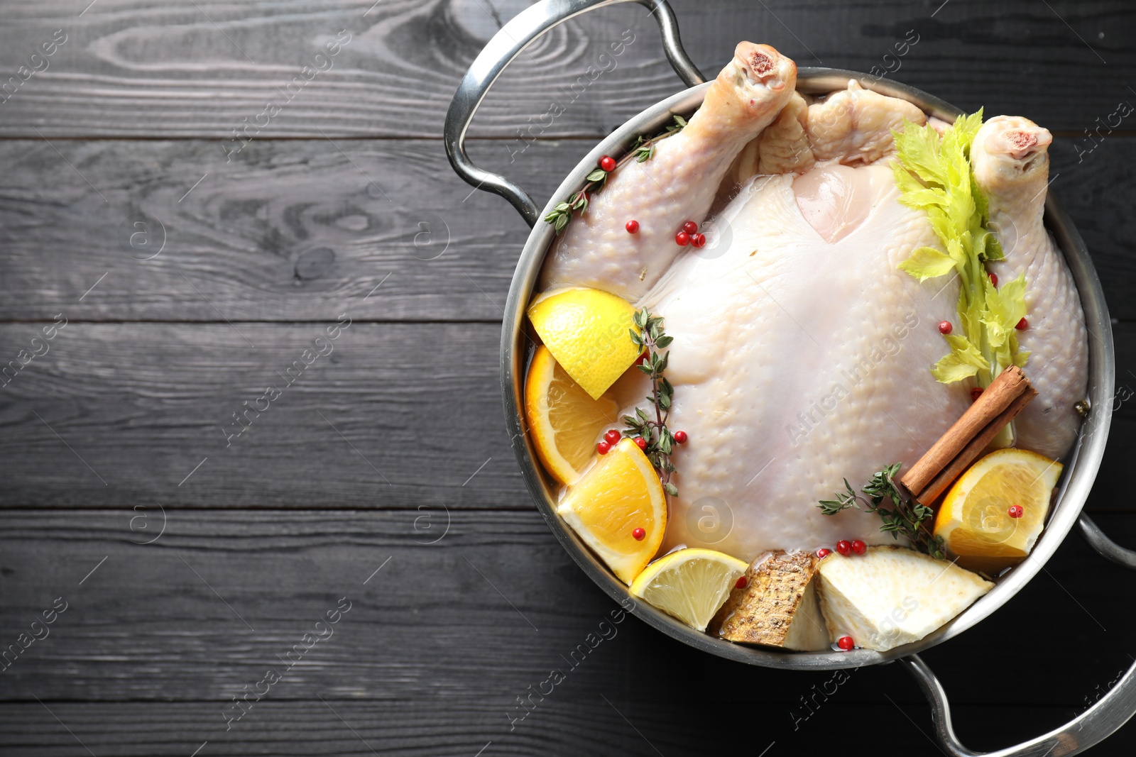 Photo of Whole raw turkey, citrus fruits and spices in pot on black wooden table, top view. Space for text