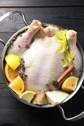 Photo of Whole raw turkey, citrus fruits and spices in pot on black wooden table, top view