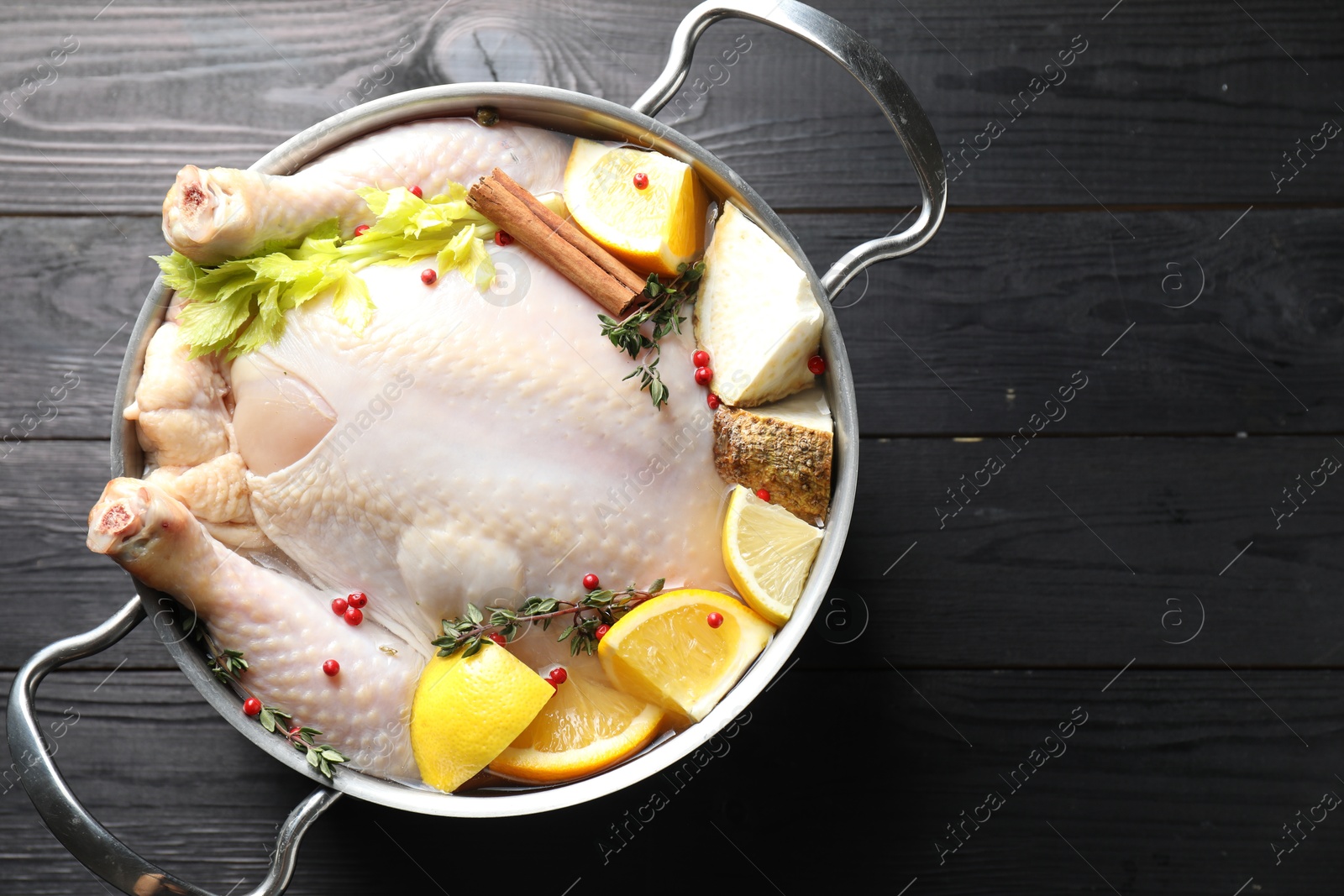 Photo of Whole raw turkey, citrus fruits and spices in pot on black wooden table, top view. Space for text