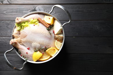 Photo of Whole raw turkey, citrus fruits and spices in pot on black wooden table, top view. Space for text