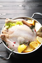 Photo of Whole raw turkey, citrus fruits and spices in pot on black wooden table, closeup