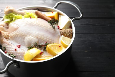 Photo of Whole raw turkey, citrus fruits and spices in pot on black wooden table, closeup. Space for text