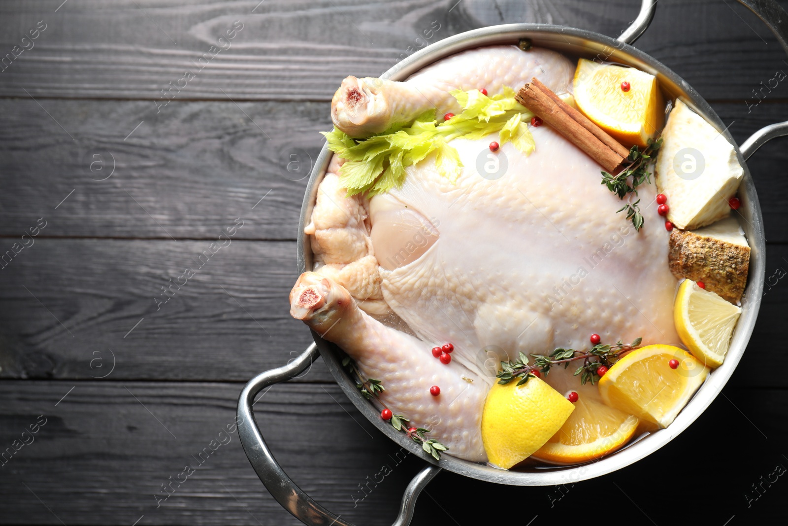 Photo of Whole raw turkey, citrus fruits and spices in pot on black wooden table, top view. Space for text