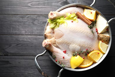 Whole raw turkey, citrus fruits and spices in pot on black wooden table, top view. Space for text