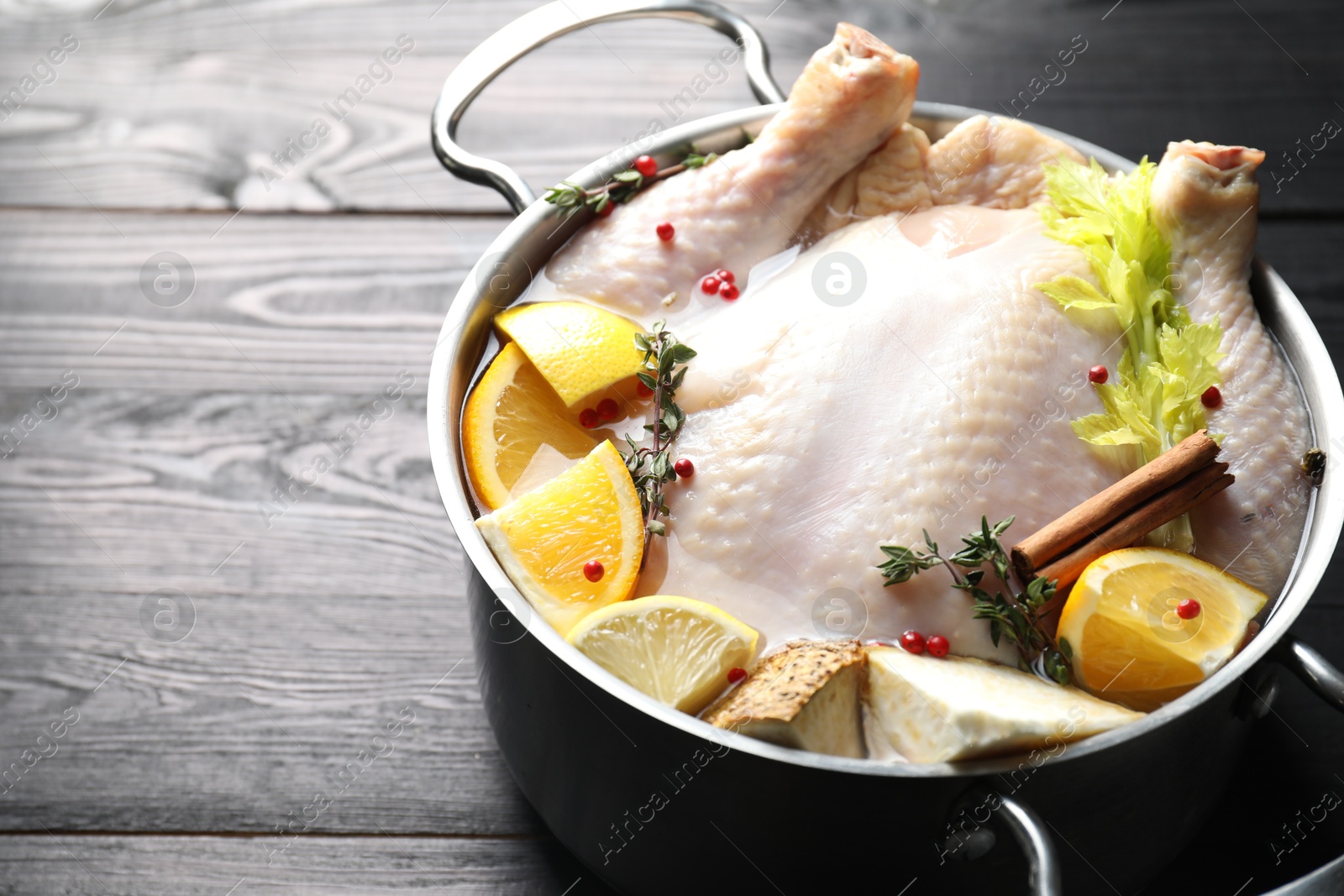 Photo of Whole raw turkey, citrus fruits and spices in pot on black wooden table, closeup. Space for text