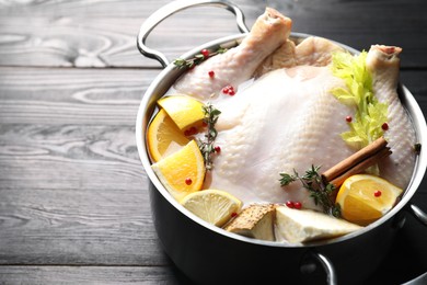 Photo of Whole raw turkey, citrus fruits and spices in pot on black wooden table, closeup. Space for text