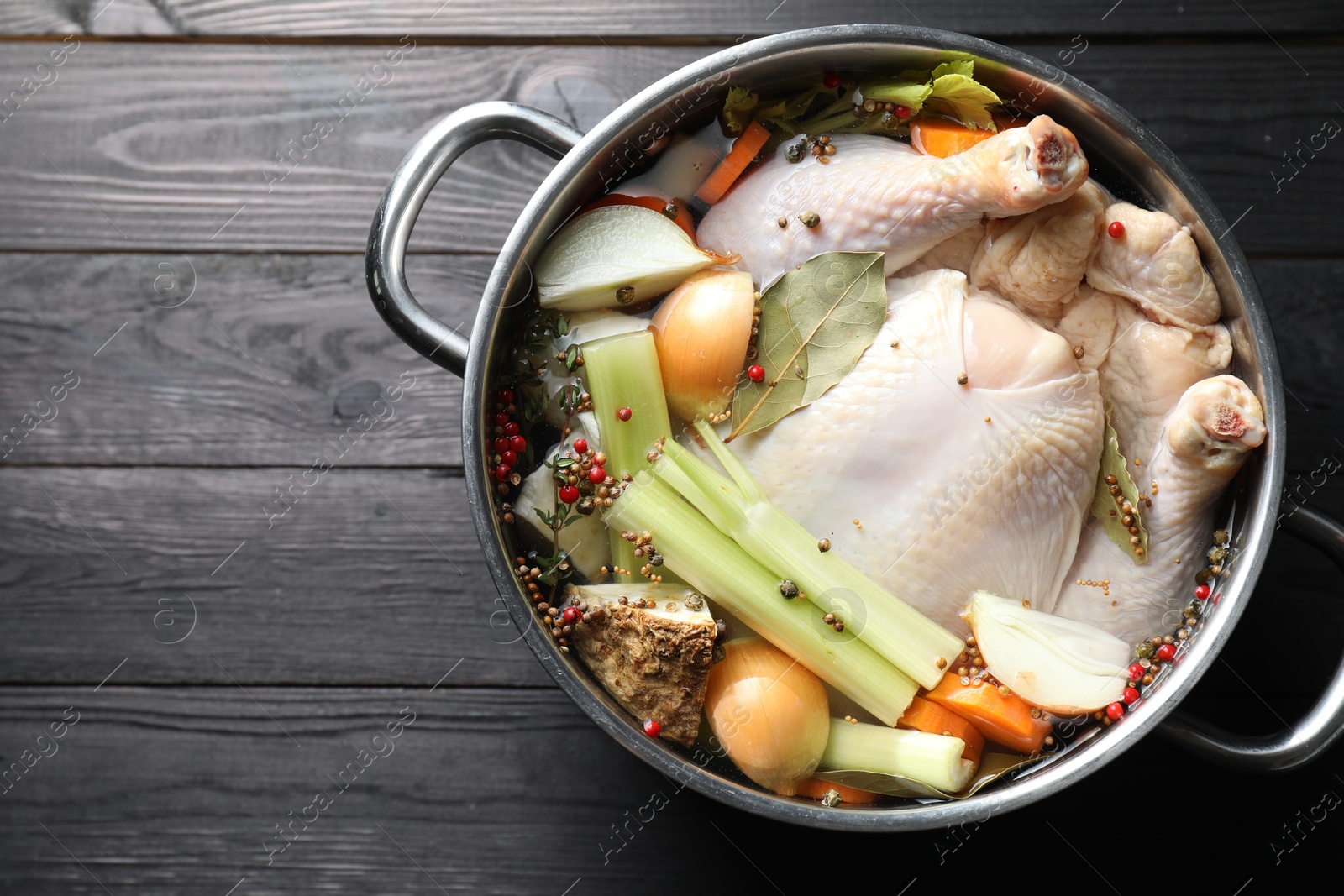 Photo of Whole raw turkey, cut onion, celery and spices in pot on black wooden table, top view. Space for text