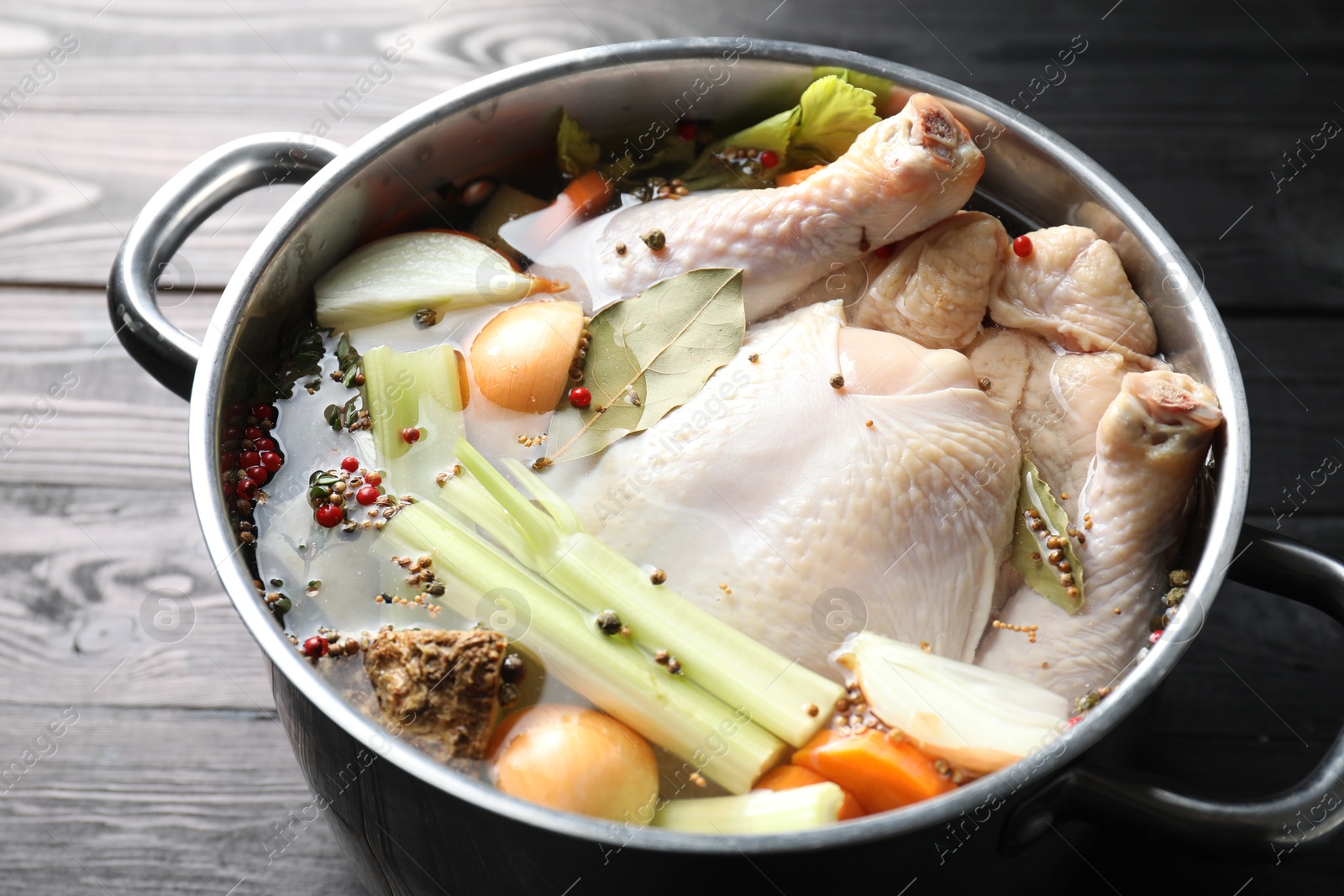 Photo of Whole raw turkey, cut onion, celery and spices in pot on black wooden table, closeup