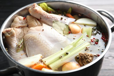 Photo of Whole raw turkey, cut onion, celery and spices in pot on black wooden table, closeup