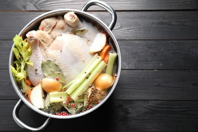 Photo of Whole raw turkey, cut onion, celery and spices in pot on black wooden table, top view. Space for text