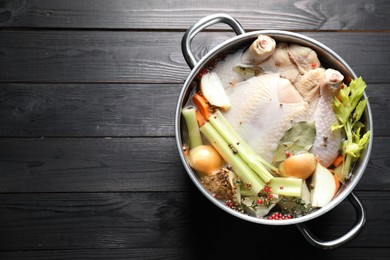 Photo of Whole raw turkey, cut onion, celery and spices in pot on black wooden table, top view. Space for text