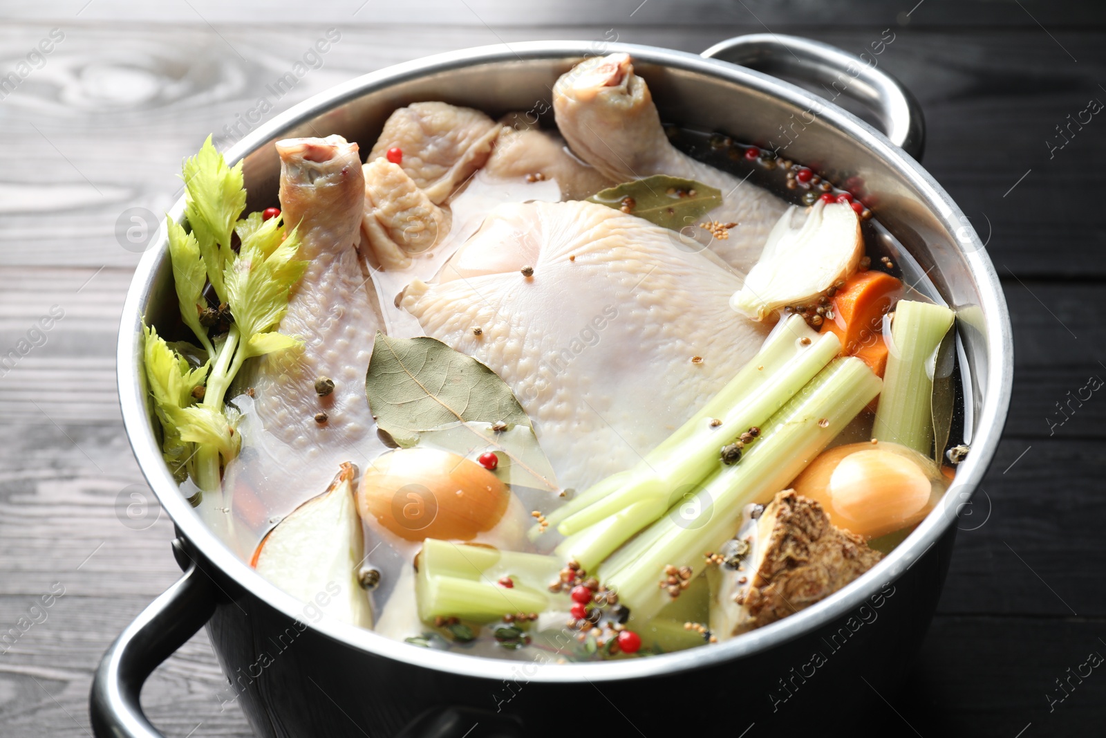 Photo of Whole raw turkey, cut onion, celery and spices in pot on black wooden table, closeup