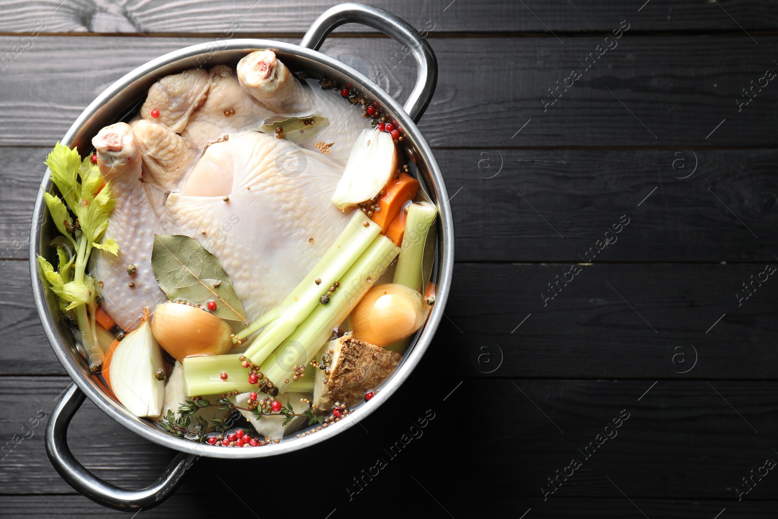 Photo of Whole raw turkey, cut onion, celery and spices in pot on black wooden table, top view. Space for text