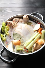 Photo of Whole raw turkey, cut onion, celery and spices in pot on black wooden table, closeup