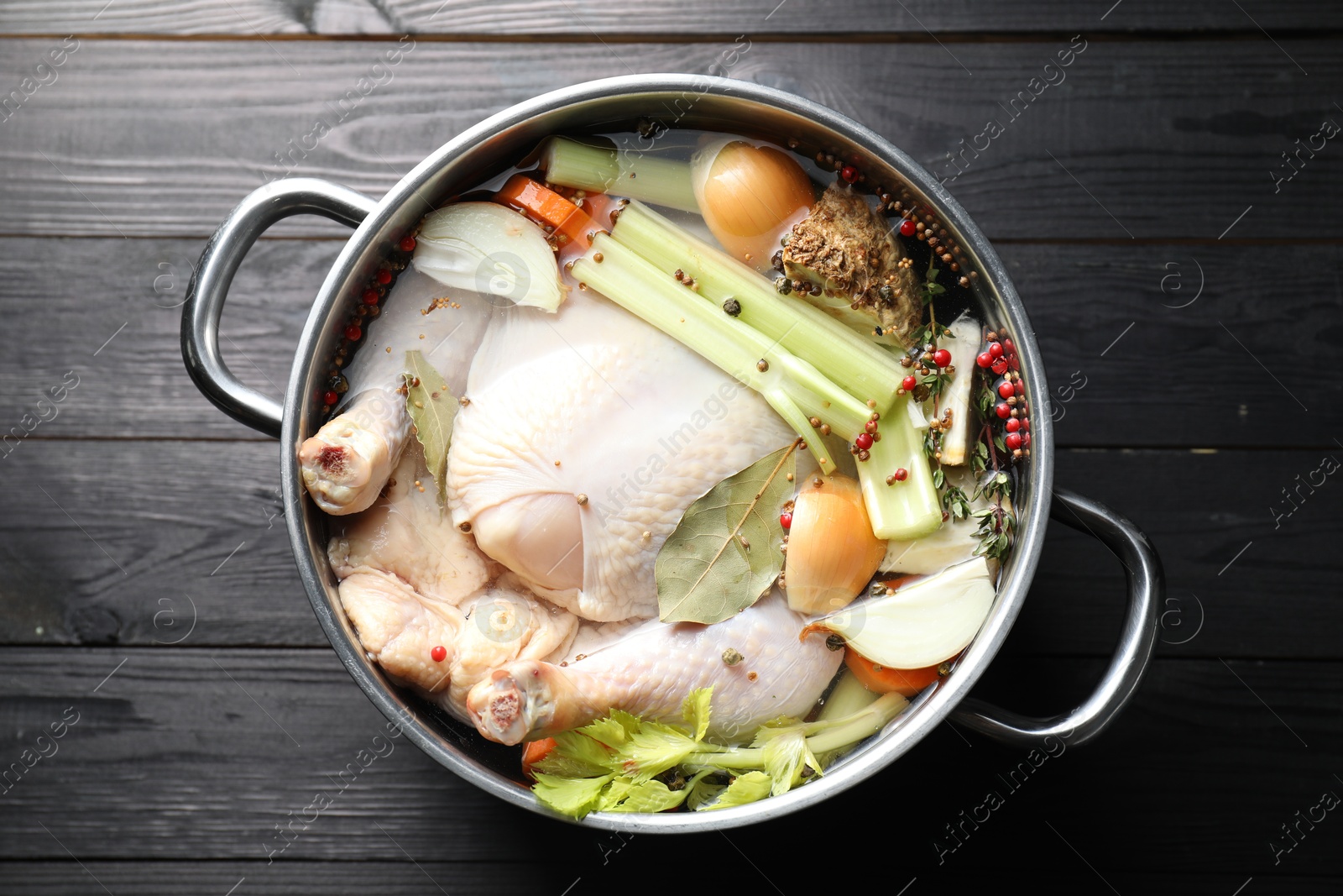 Photo of Whole raw turkey, cut onion, celery and spices in pot on black wooden table, top view