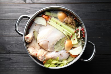 Photo of Whole raw turkey, cut onion, celery and spices in pot on black wooden table, top view