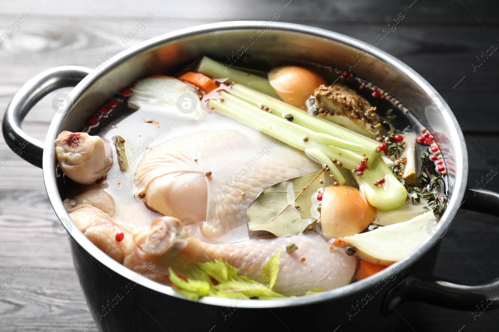 Photo of Whole raw turkey, cut onion, celery and spices in pot on black wooden table, closeup