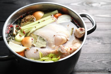 Photo of Whole raw turkey, cut onion, celery and spices in pot on black wooden table, closeup