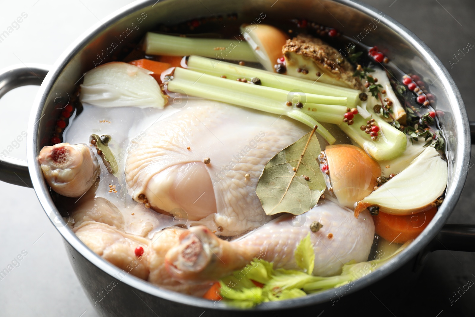 Photo of Whole raw turkey, cut onion, celery and spices in pot on grey table, closeup