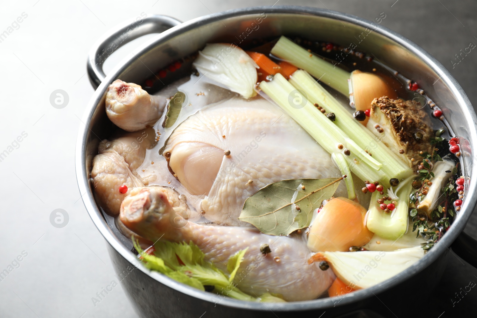 Photo of Whole raw turkey, cut onion, celery and spices in pot on grey table, closeup