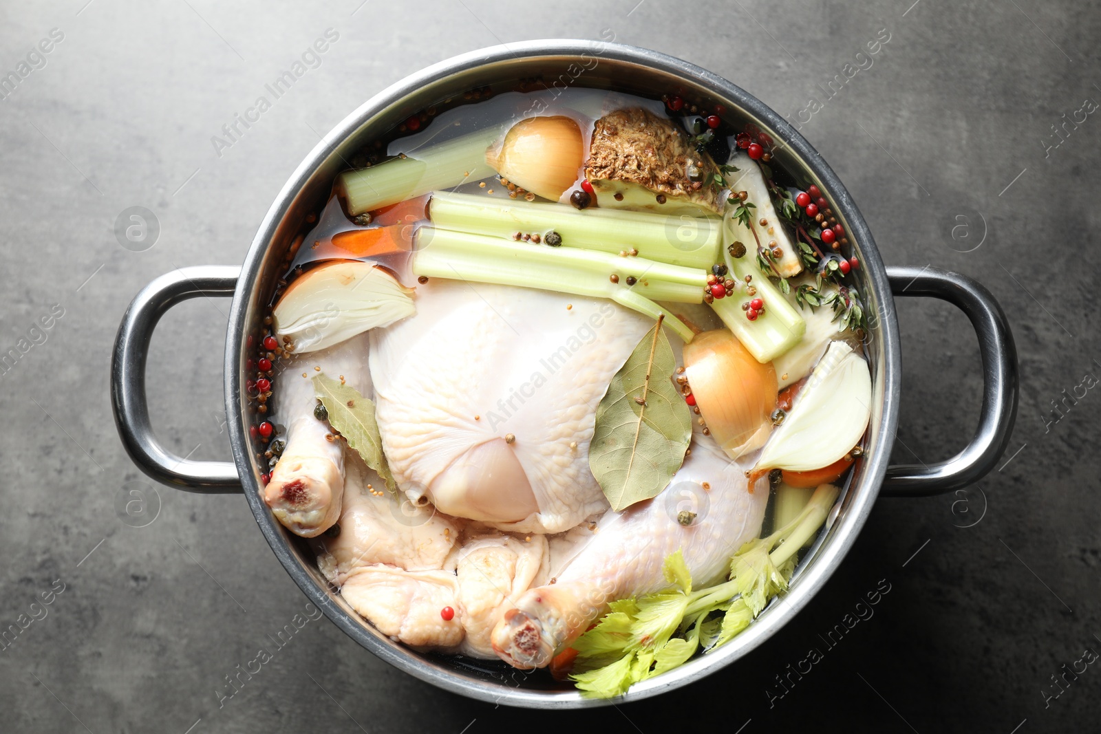 Photo of Whole raw turkey, cut onion, celery and spices in pot on grey textured table, top view