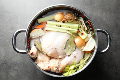 Photo of Whole raw turkey, cut onion, celery and spices in pot on grey textured table, top view