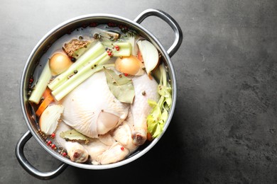 Photo of Whole raw turkey, cut onion, celery and spices in pot on grey textured table, top view. Space for text