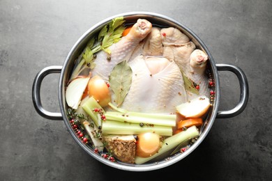 Photo of Whole raw turkey, cut onion, celery and spices in pot on grey textured table, top view