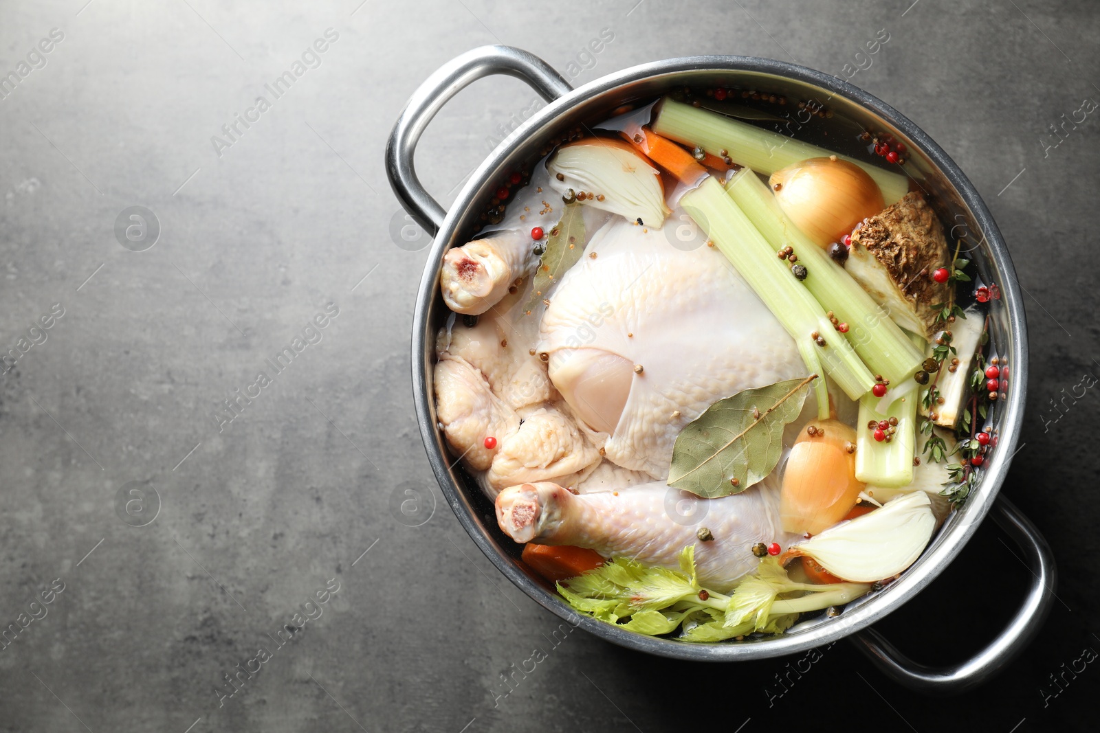 Photo of Whole raw turkey, cut onion, celery and spices in pot on grey textured table, top view. Space for text