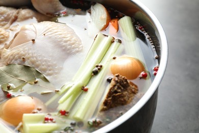 Photo of Whole raw turkey, cut onion, celery and spices in pot on grey table, closeup