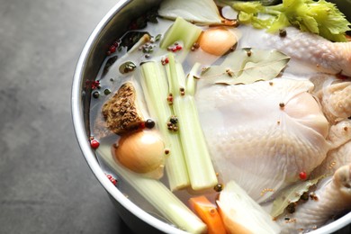 Photo of Whole raw turkey, cut onion, celery and spices in pot on grey table, closeup