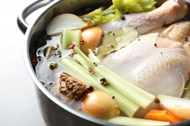 Photo of Whole raw turkey, cut onion, celery and spices in pot on light background, closeup