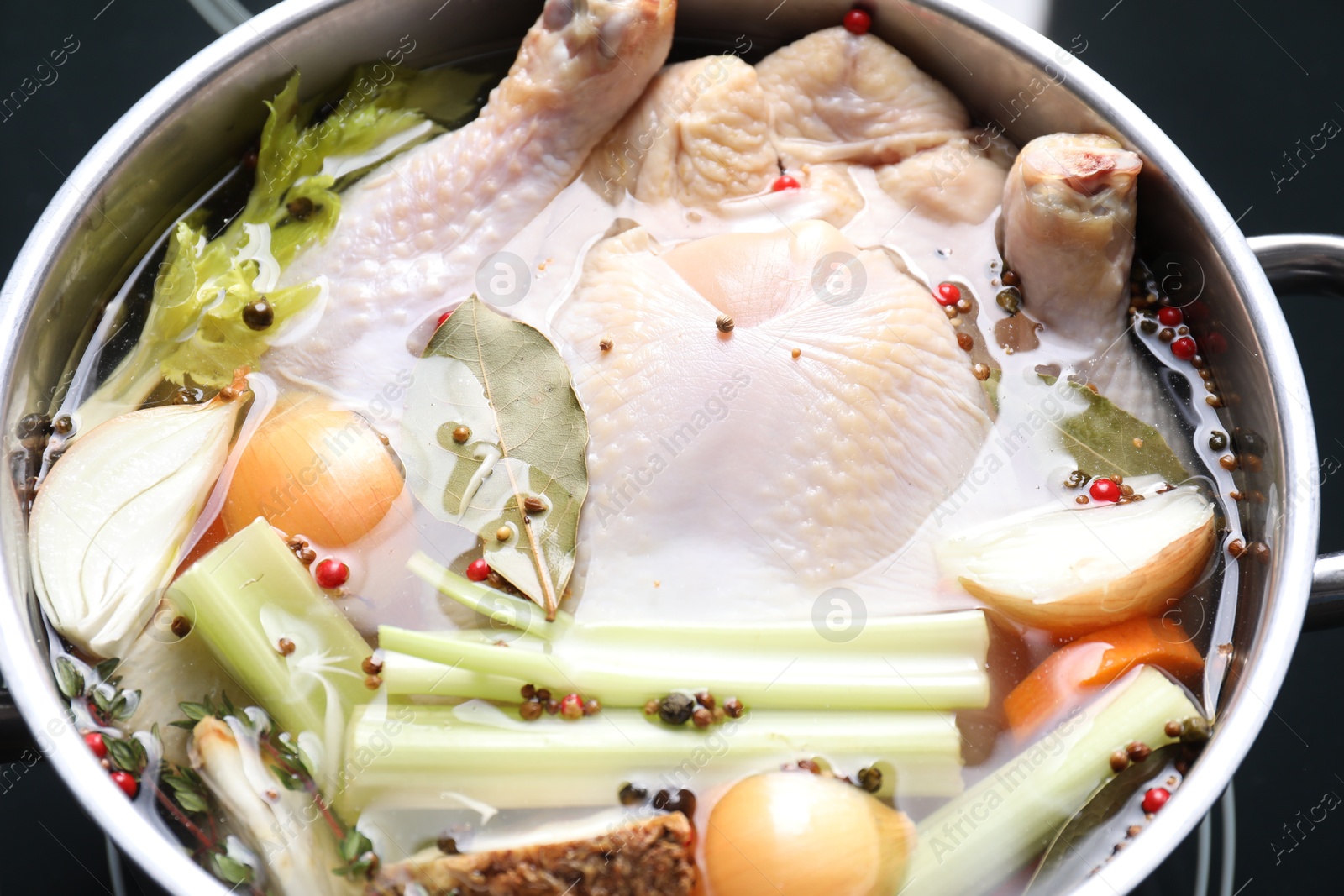 Photo of Whole raw turkey, cut onion, celery and spices in pot, closeup